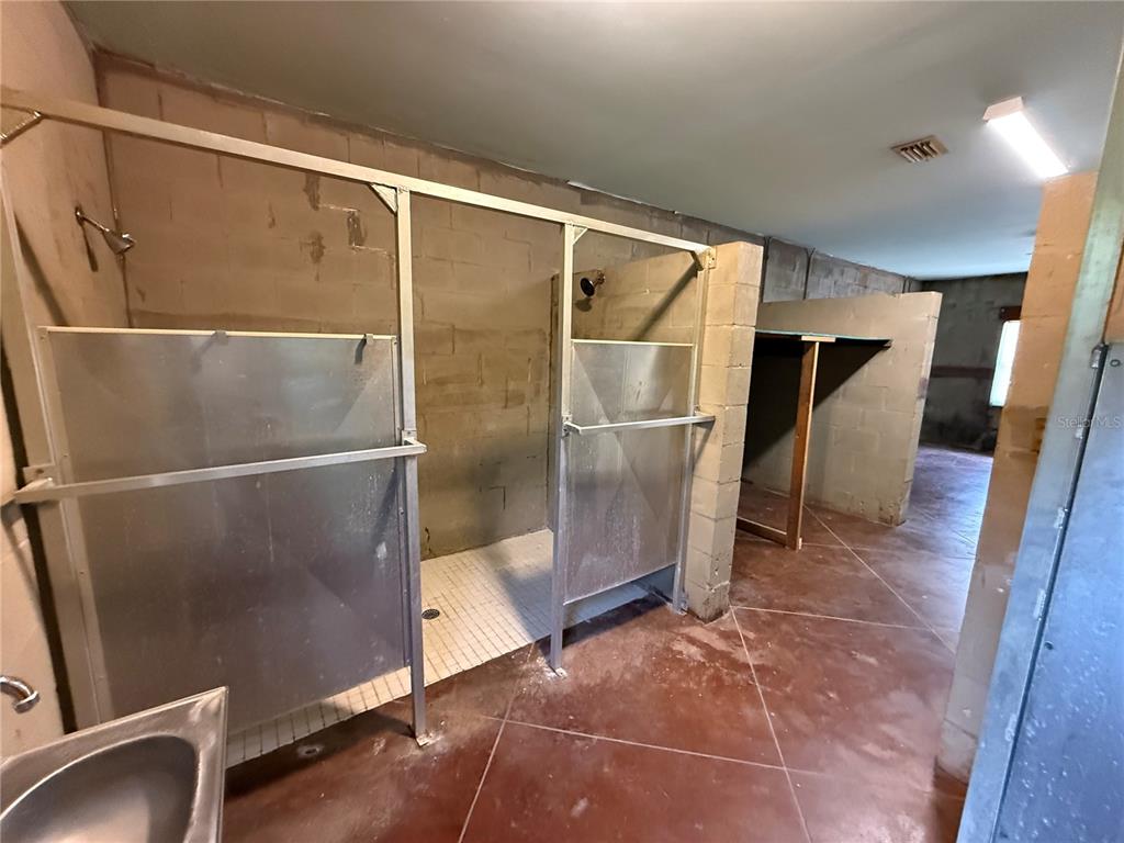 This room features multiple shower stalls with metal partitions and exposed concrete block walls — 2308 FERN PALM DRIVE, EDGEWATER, FL