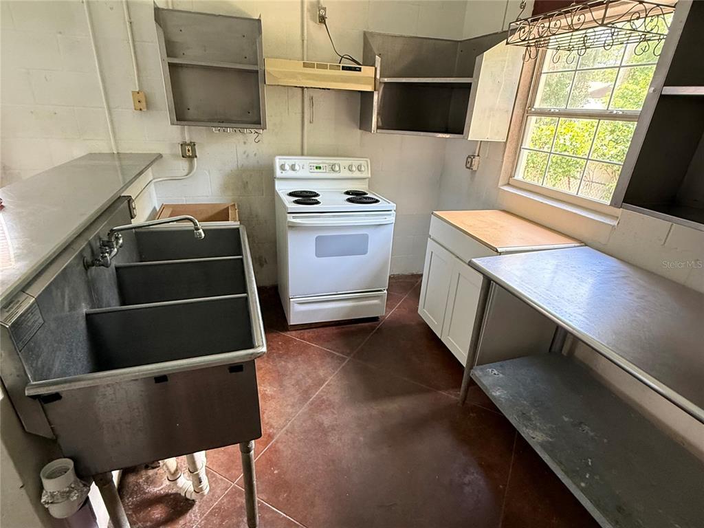 A kitchen features a three-compartment stainless steel sink, a white stove, and metal shelving — 2308 FERN PALM DRIVE, EDGEWATER, FL