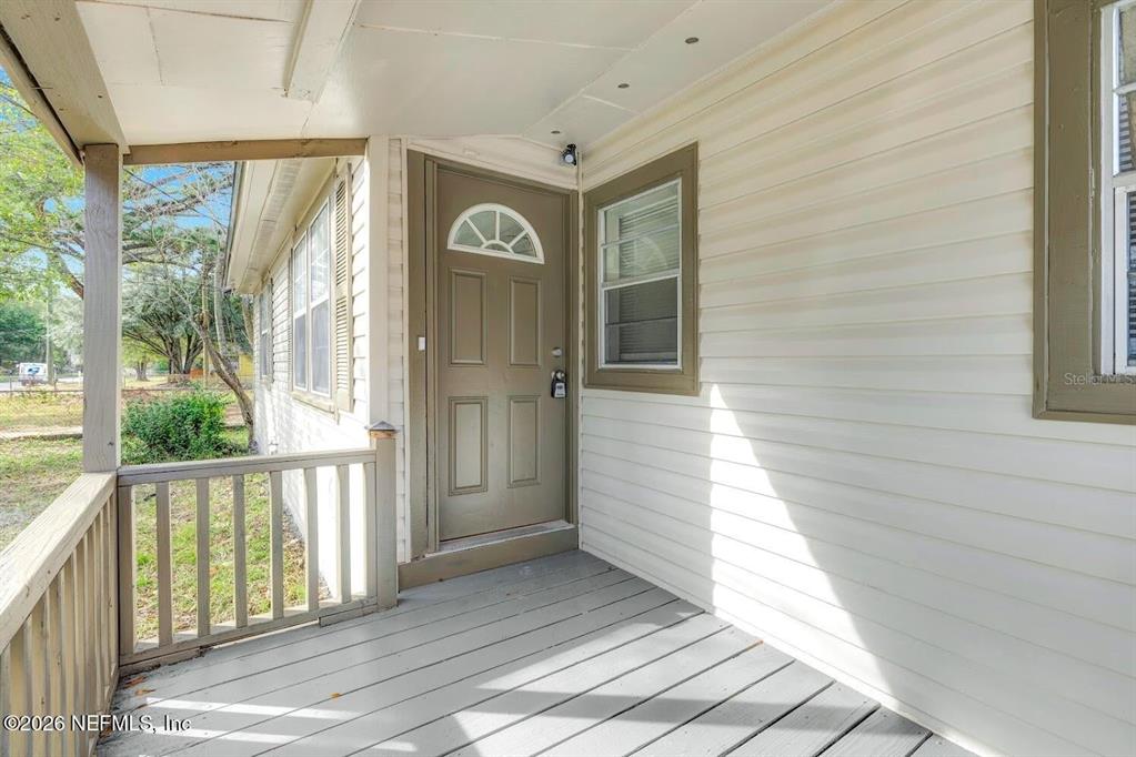 A covered wooden porch features a tan front door and light-colored horizontal siding — 2971 W 16TH STREET, JACKSONVILLE, FL