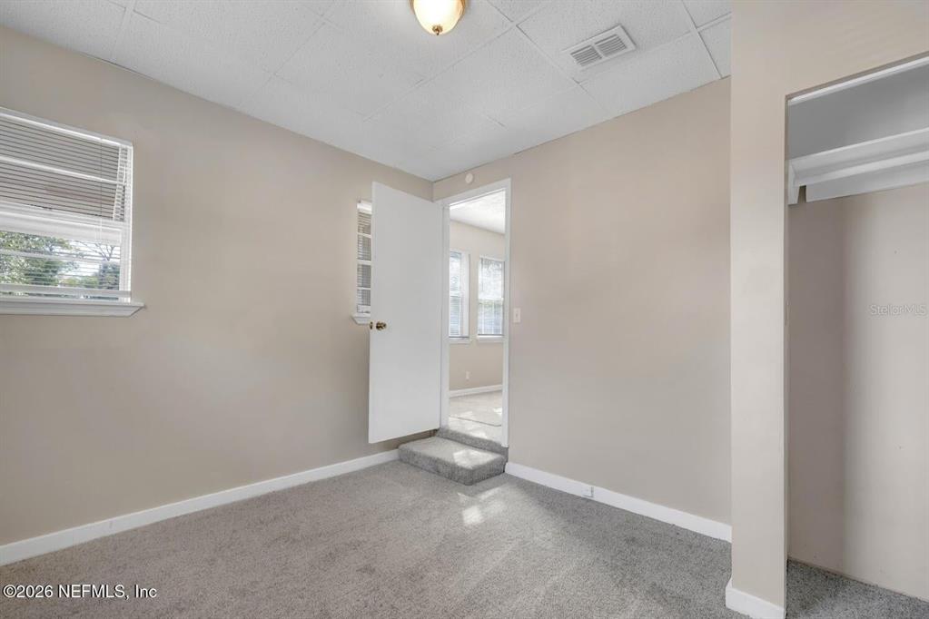 A carpeted bedroom features a window, a closet, and a doorway leading to another room — 2971 W 16TH STREET, JACKSONVILLE, FL