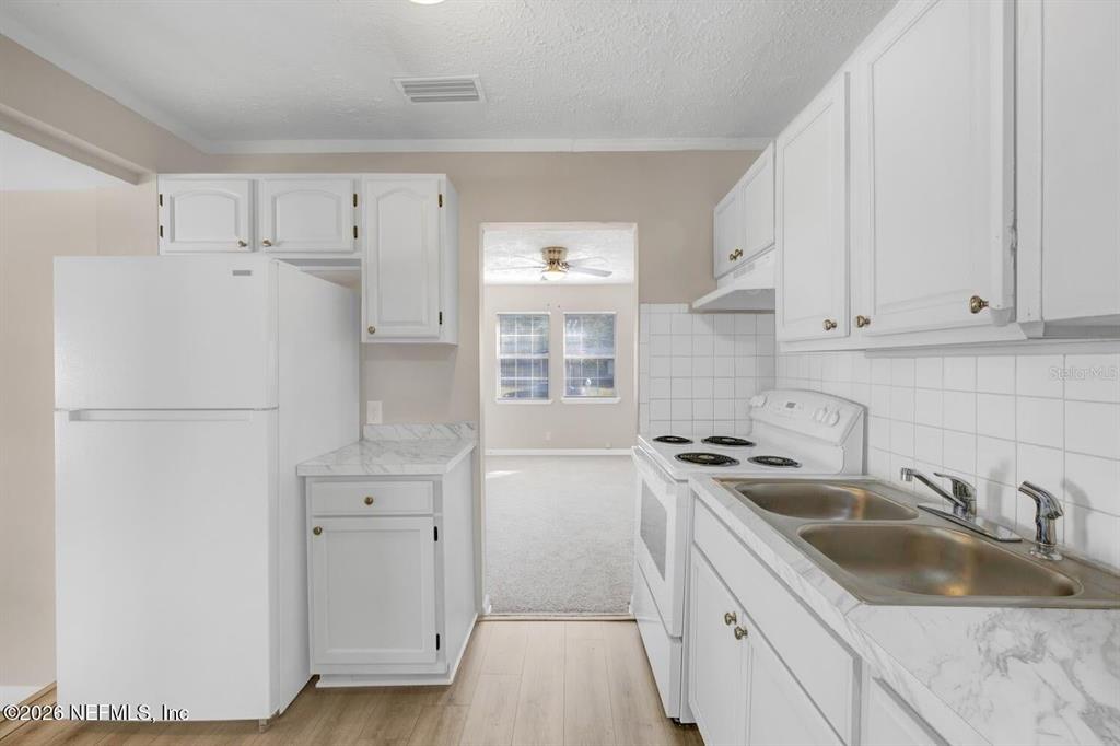 A kitchen features white cabinets, a white refrigerator, a white stove, and a stainless sink — 2971 W 16TH STREET, JACKSONVILLE, FL