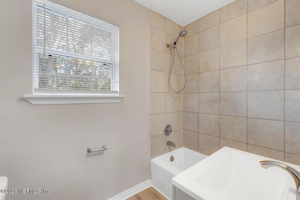 A bathroom features a tiled shower-tub combination, a window, and a white vanity sink — 2971 W 16TH STREET, JACKSONVILLE, FL
