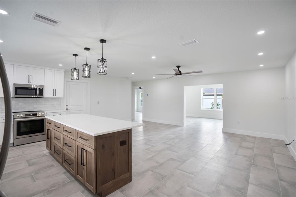 A kitchen with white cabinets, a wood island, and tile flooring opens into a living area — 5528 BRIARCLIFF DRIVE, SARASOTA, FL