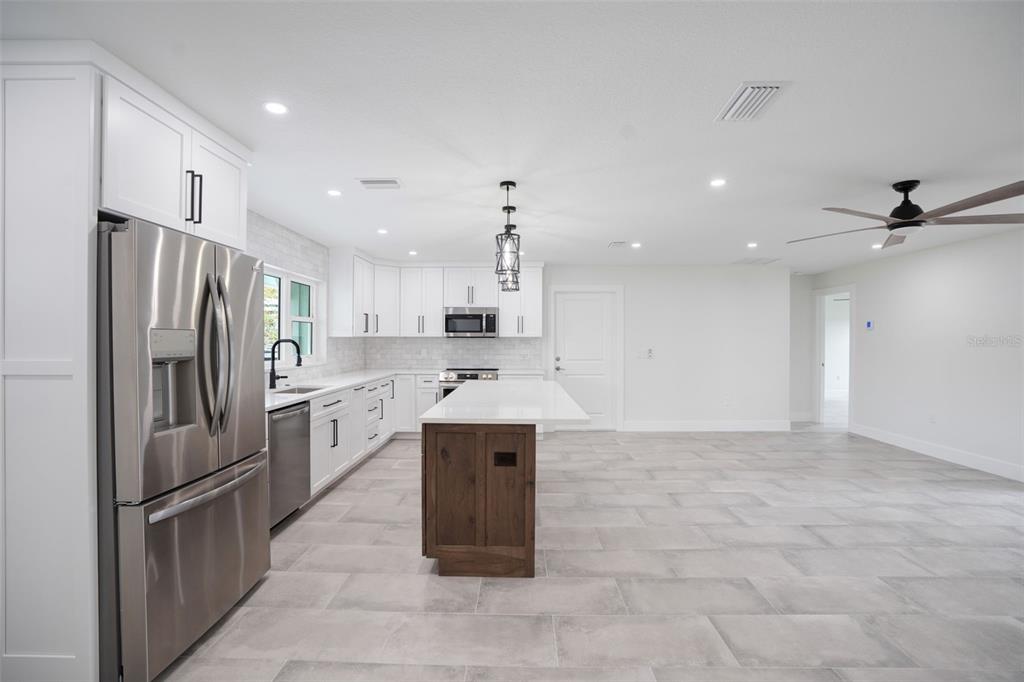 A modern kitchen features white cabinetry, a wood-toned island, stainless steel appliances, and tile flooring — 5528 BRIARCLIFF DRIVE, SARASOTA, FL