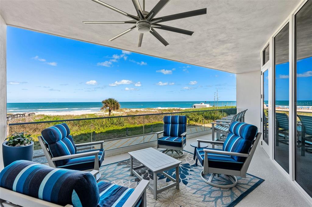 A covered balcony features blue striped patio furniture, a patterned rug, and ocean views — 65 N ATLANTIC AVENUE UNIT 205, COCOA BEACH, FL