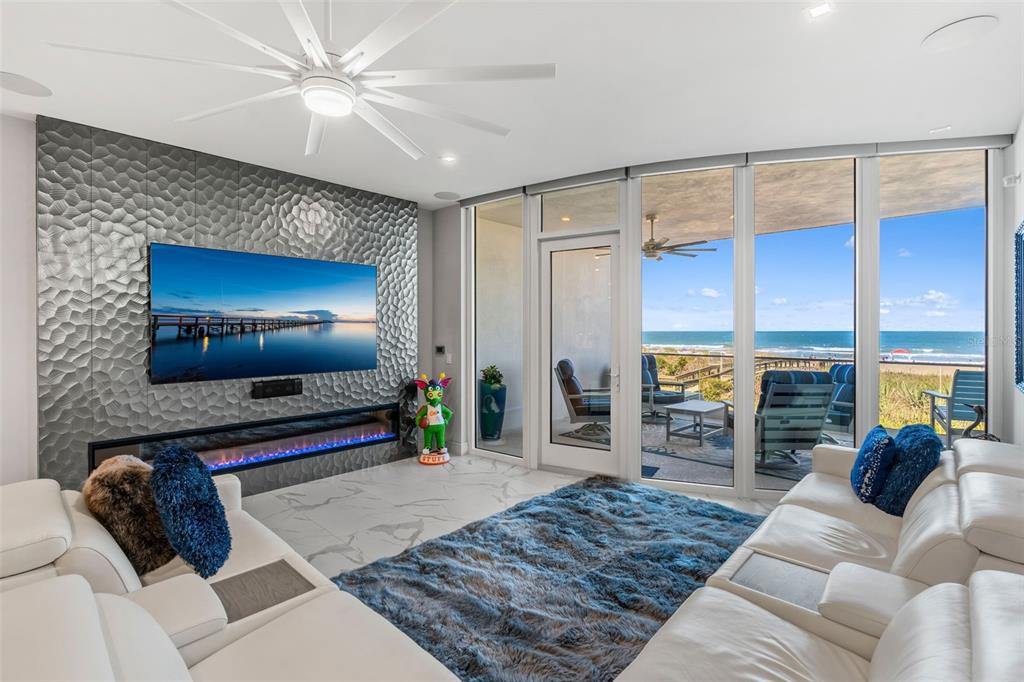 A living room features a textured accent wall, linear fireplace, white sofas, and ocean views — 65 N ATLANTIC AVENUE UNIT 205, COCOA BEACH, FL