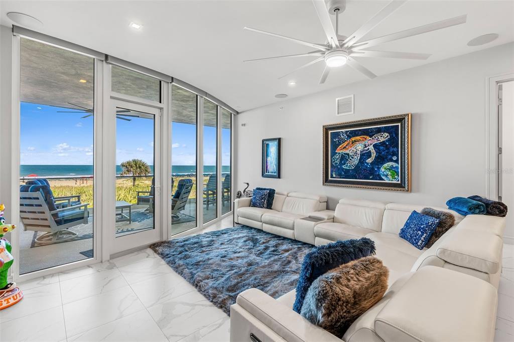 A living room with white leather sofas, a blue shag rug, and floor-to-ceiling ocean views — 65 N ATLANTIC AVENUE UNIT 205, COCOA BEACH, FL