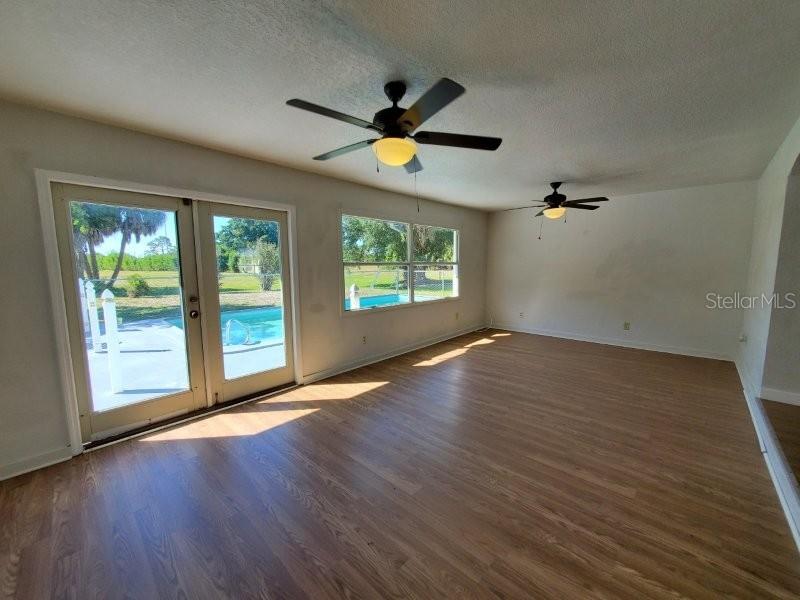 A living room with wood-look flooring, two ceiling fans, and glass doors opening to a pool — 2451 AQUILOS COURT, PORT CHARLOTTE, FL