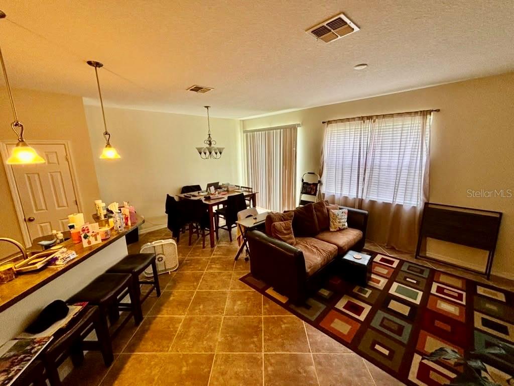 An open-concept living and dining area features tile flooring, a brown sofa, and pendant lighting — 3605 SPECKLED WAY, SANFORD, FL