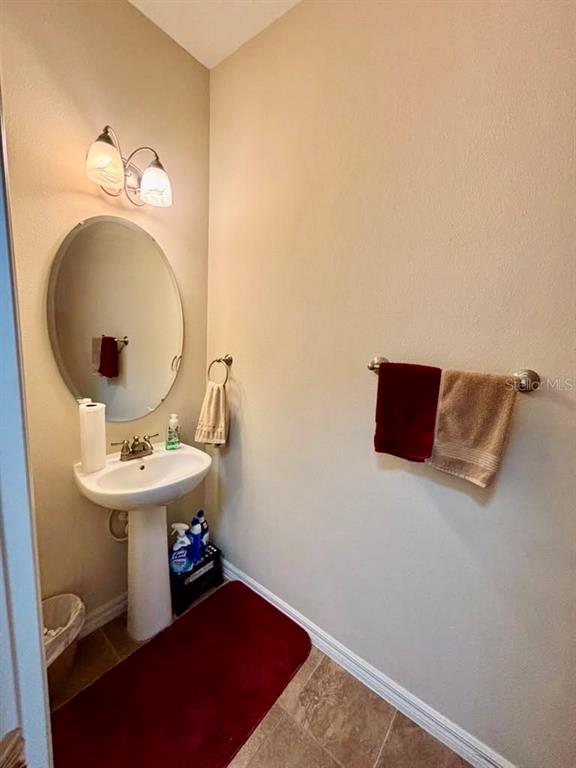 A small powder room features a pedestal sink, oval mirror, and red accent towels — 3605 SPECKLED WAY, SANFORD, FL