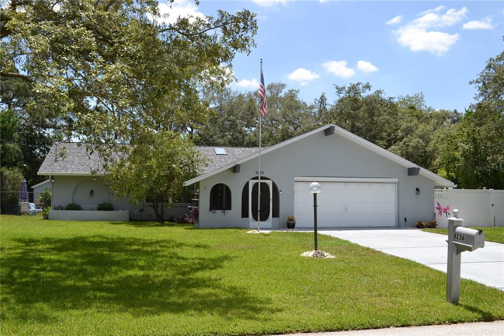 A single-story gray house with a two-car garage, a front lawn, and an American flag — 8236 ANNAPOLIS ROAD, SPRING HILL, FL