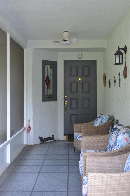 A covered porch features a gray front door, wicker chairs, and a ceiling fan — 8236 ANNAPOLIS ROAD, SPRING HILL, FL