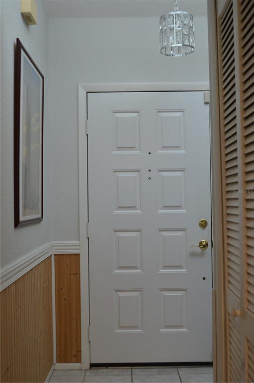 An entryway features a white paneled door, wood wainscoting, a framed picture, and a crystal chandelier — 8236 ANNAPOLIS ROAD, SPRING HILL, FL