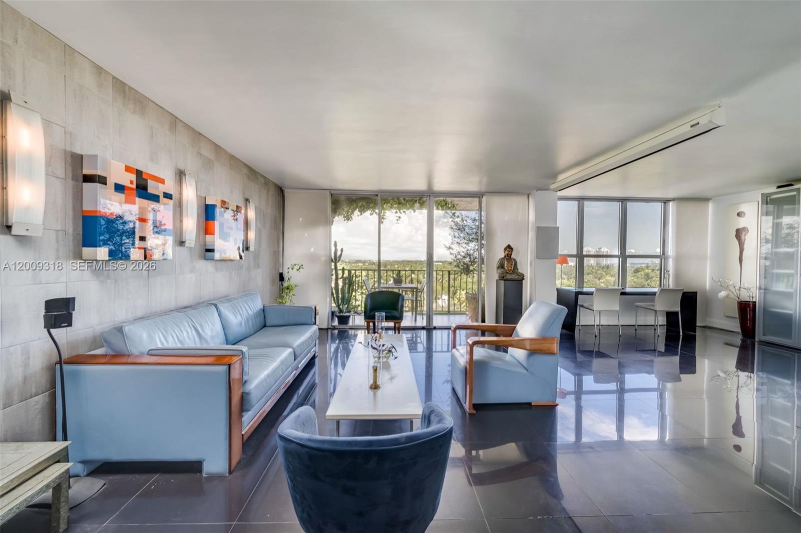 A modern living room features light blue leather furniture, dark tile floors, and a balcony view — 780 NE 69th St # 808, Miami FL 33138, MIAMI, FL