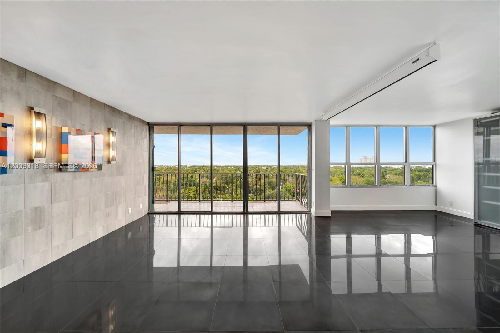 A bright living room features dark tile flooring, a textured accent wall, and floor-to-ceiling windows — 780 NE 69th St # 808, Miami FL 33138, MIAMI, FL