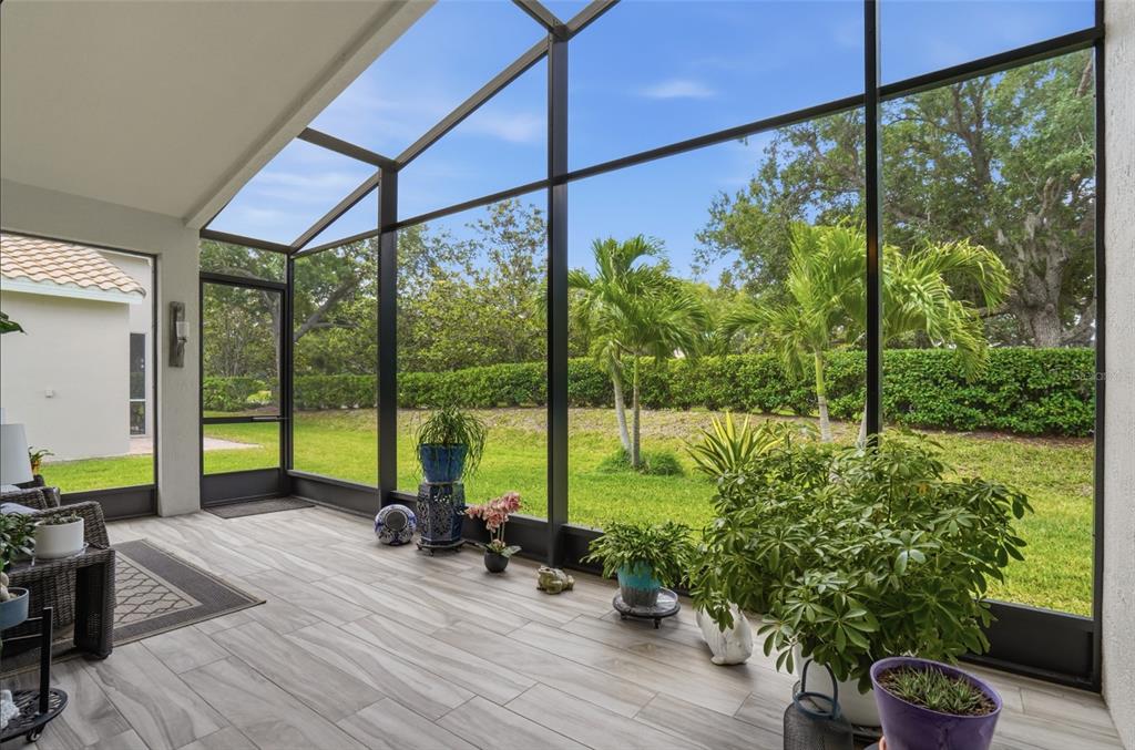 A screened-in patio with tile flooring overlooks a grassy backyard with palm trees and hedges — 4222 65TH PLACE E, SARASOTA, FL
