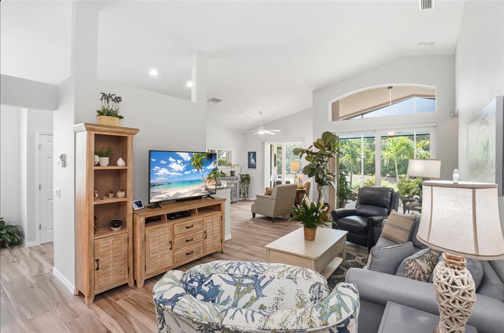 A bright living room features light wood-look flooring, vaulted ceilings, and a view of the patio — 4222 65TH PLACE E, SARASOTA, FL