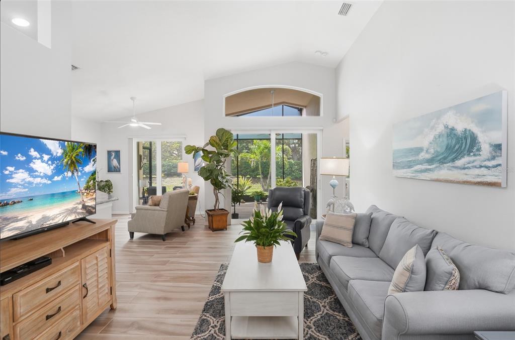 A bright living room features a grey sofa, a wooden media console, and sliding glass doors — 4222 65TH PLACE E, SARASOTA, FL