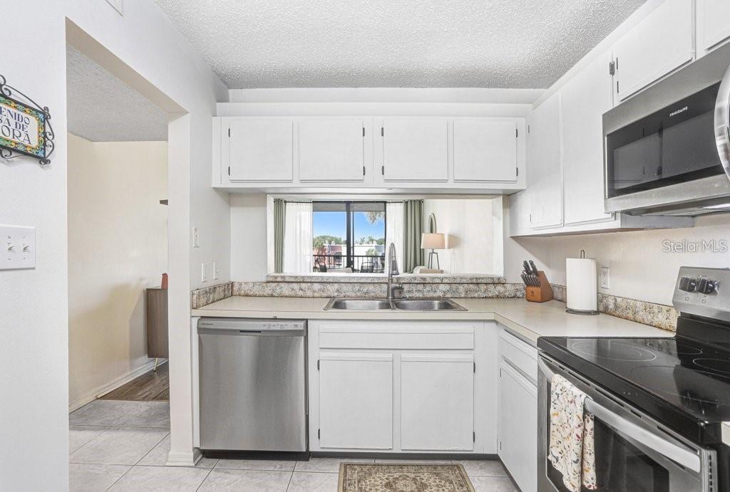A kitchen features white cabinets, stainless steel appliances, and a pass-through window to the living area — 2424 W TAMPA BAY BOULEVARD UNIT M205, TAMPA, FL