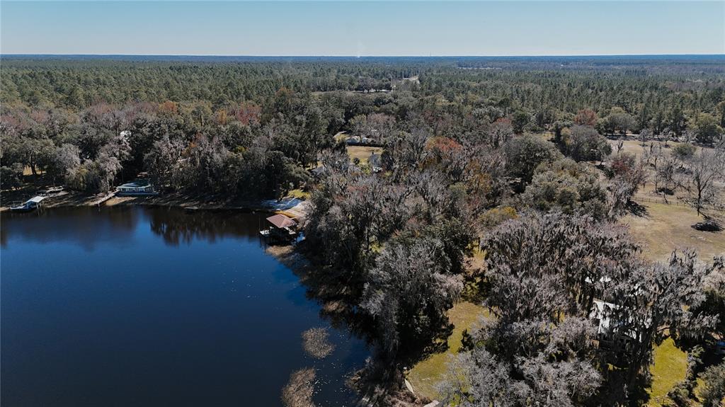 An aerial view shows a lake with docks surrounded by dense trees and vegetation — 16970 NE 120TH AVENUE, WALDO, FL