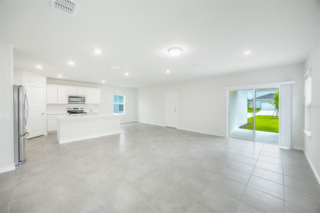 A bright, open-concept kitchen and living area with white cabinets, tile floors, and sliding doors — 6090 WINDY LEAF ALLEY, ST CLOUD, FL