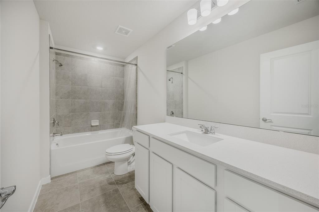 A bathroom features a white vanity, a large mirror, and a gray tiled shower-tub combination — 6090 WINDY LEAF ALLEY, ST CLOUD, FL