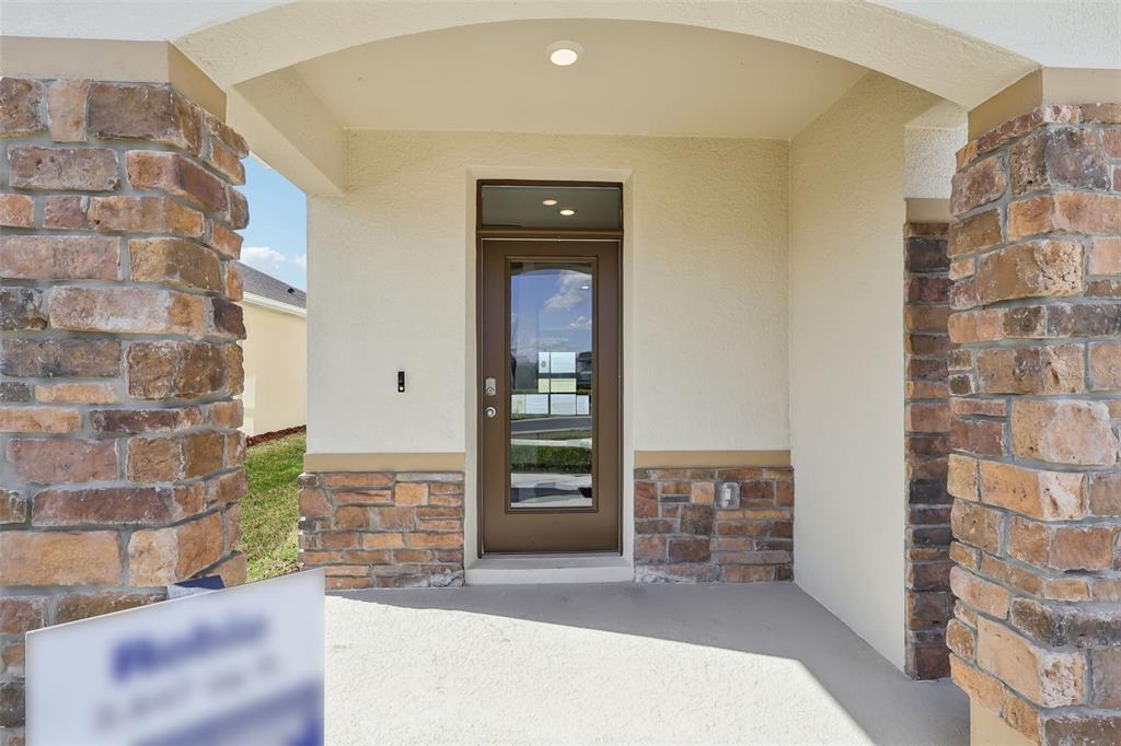 A covered entryway features stone pillars, a tan stucco wall, and a glass-paneled front door — 1189 CUMBERLAND TRAIL DRIVE, LAKE HAMILTON, FL