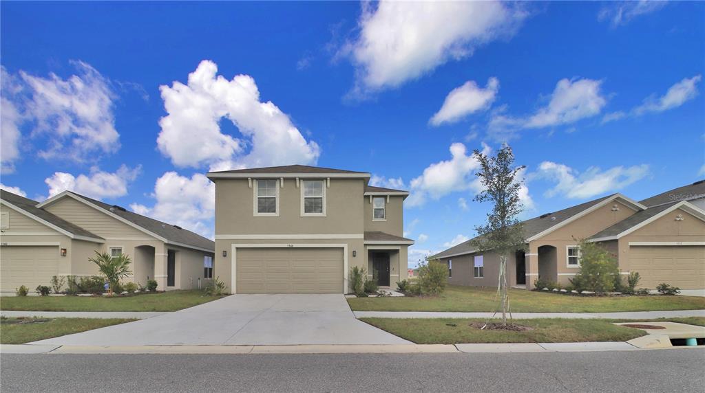 A two-story suburban house with a tan exterior, a two-car garage, and a concrete driveway — 5546 LOGAN CAVE AVENUE, WIMAUMA, FL