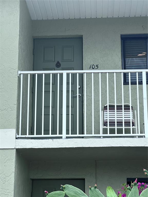 A second-story balcony features a green door numbered 105, a white railing, and a chair — 25225 RAMPART BOULEVARD UNIT 105, PUNTA GORDA, FL