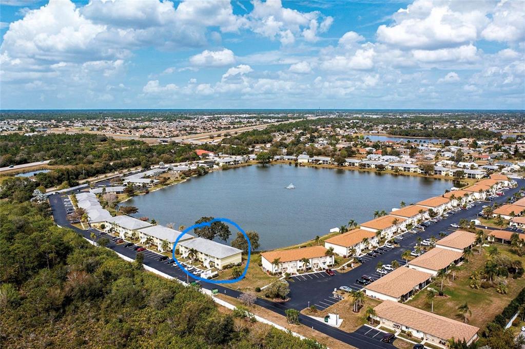 An aerial view shows a multi-unit residential building circled in blue beside a lake — 25225 RAMPART BOULEVARD UNIT 105, PUNTA GORDA, FL