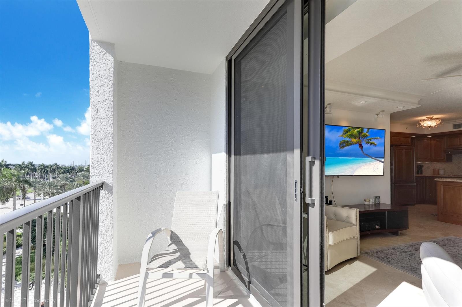 A balcony with a chair overlooks a palm-lined landscape, adjacent to an open-concept living area — 651 Okeechobee Boulevard # 509, West Palm Beach FL 33401, WEST PALM BEACH, FL