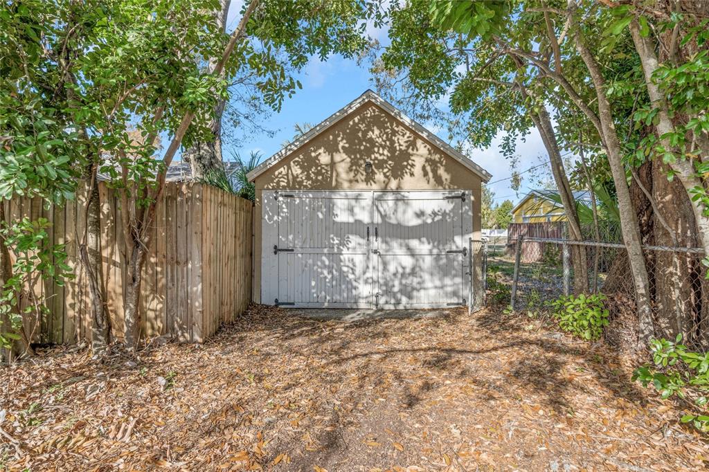 A detached garage with white double doors stands in a yard surrounded by trees — 4139 26TH STREET N, ST PETERSBURG, FL