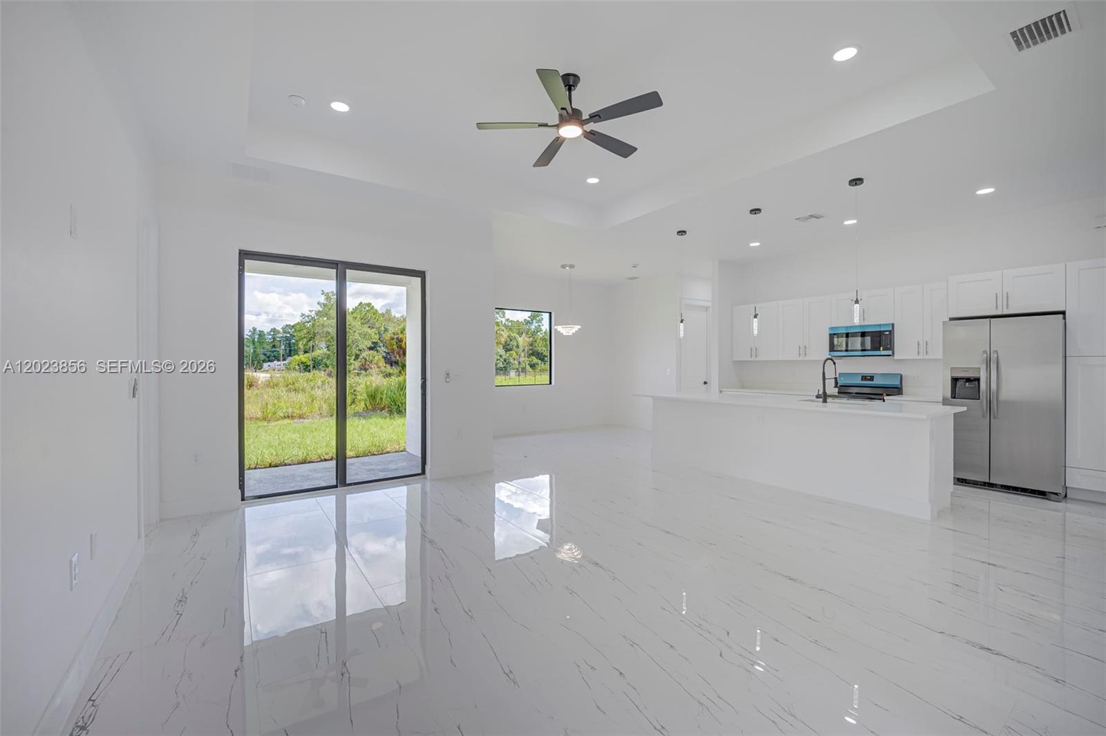 A bright, open-concept kitchen and living area features white cabinetry, stainless appliances, and marble-look flooring — 931 BARCELONA ST E, Lehigh Acres FL 33974, LEHIGH ACRES, FL