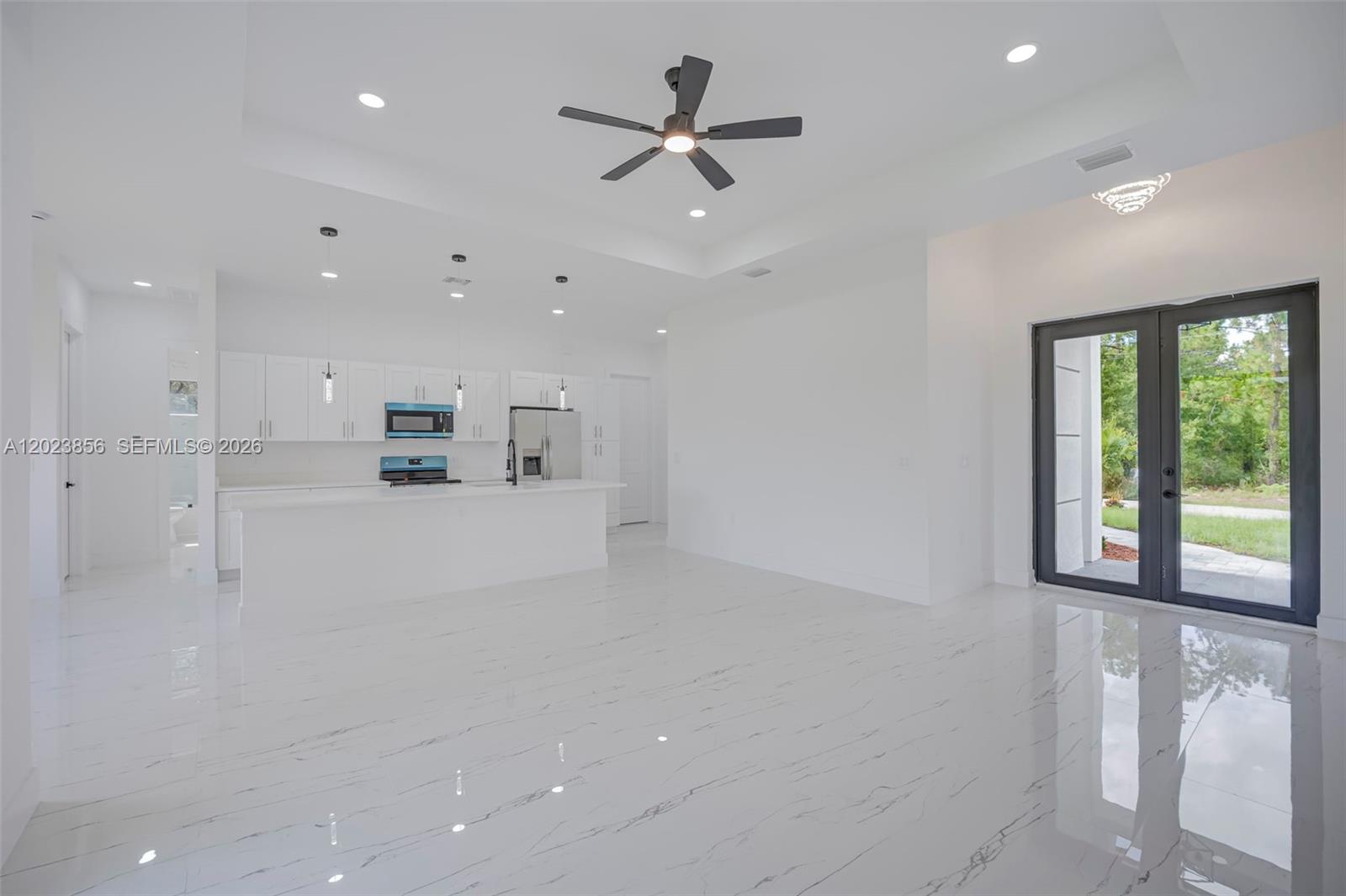 A modern, open-concept kitchen and living area features white cabinetry, marble-look flooring, and glass doors — 931 BARCELONA ST E, Lehigh Acres FL 33974, LEHIGH ACRES, FL