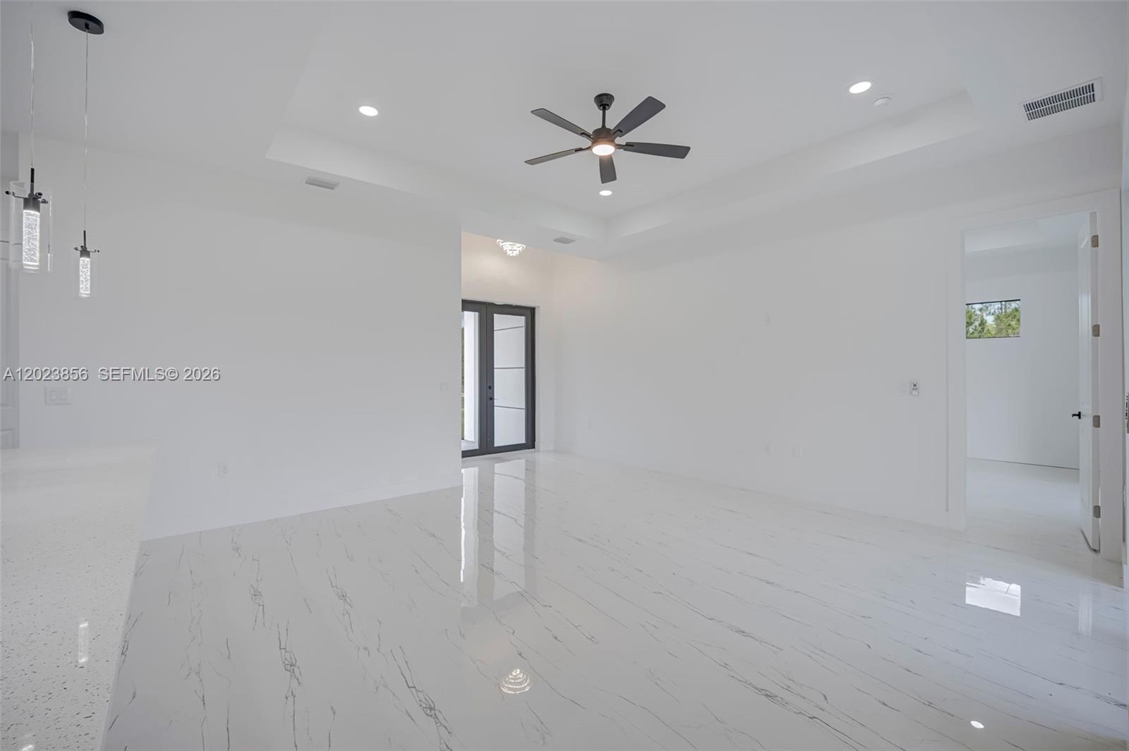 A bright, minimalist room features white walls, a tray ceiling with a fan, and marble-patterned flooring — 931 BARCELONA ST E, Lehigh Acres FL 33974, LEHIGH ACRES, FL