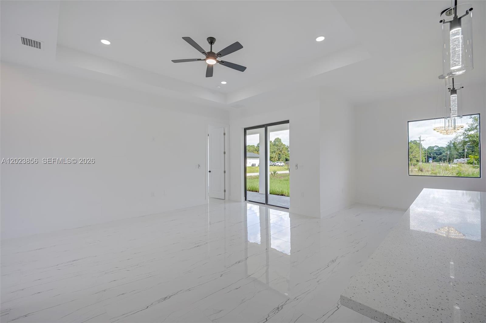 A bright, open-concept room features white marble-look tile flooring, a tray ceiling, and sliding glass doors — 931 BARCELONA ST E, Lehigh Acres FL 33974, LEHIGH ACRES, FL