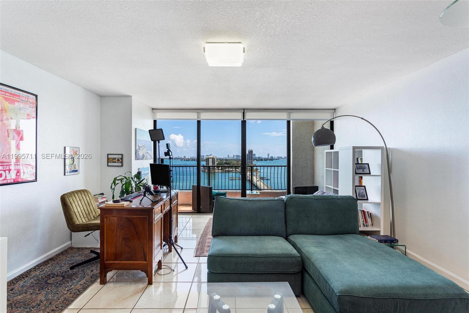 A living room with a desk, teal sectional sofa, and a balcony overlooking the water — 555 NE 15th St # 15B, Miami FL 33132, MIAMI, FL