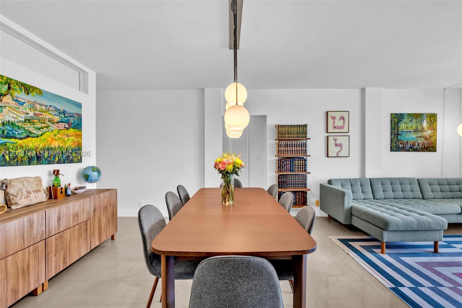 A dining room features a long wooden table, grey chairs, and a nearby blue sofa — 9381 E Bay Harbor Dr # 202s, Bay Harbor Islands FL 33154, BAY HARBOR ISLANDS, FL