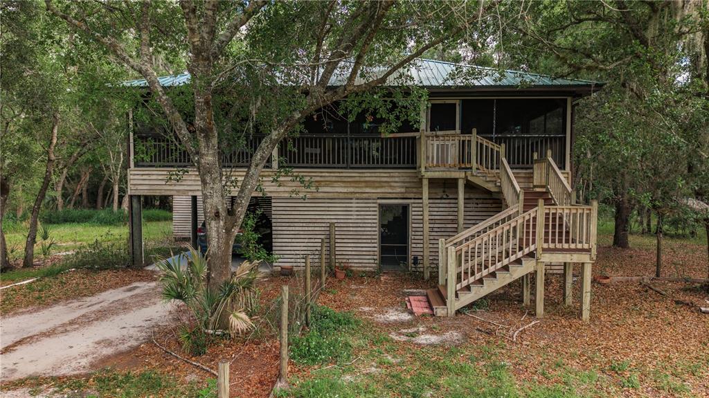 A two-story house on stilts features a screened-in porch and an exterior wooden staircase — 8056 SW HORSE CREEK ROAD, ARCADIA, FL