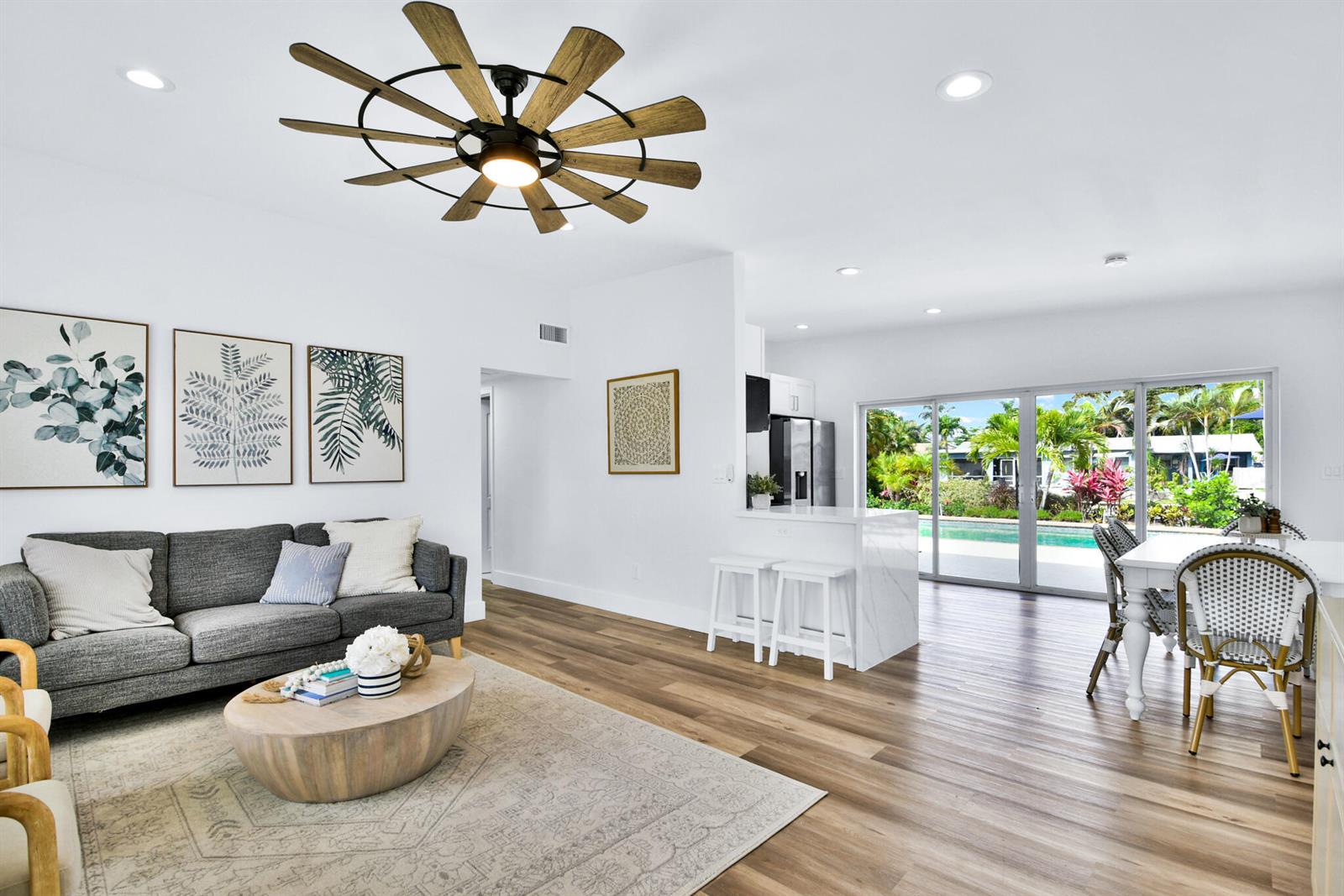 A bright living and dining area features wood-look flooring, a gray sofa, and pool views — 6821 Kingston Drive, Lake Worth FL 33462, LAKE WORTH, FL
