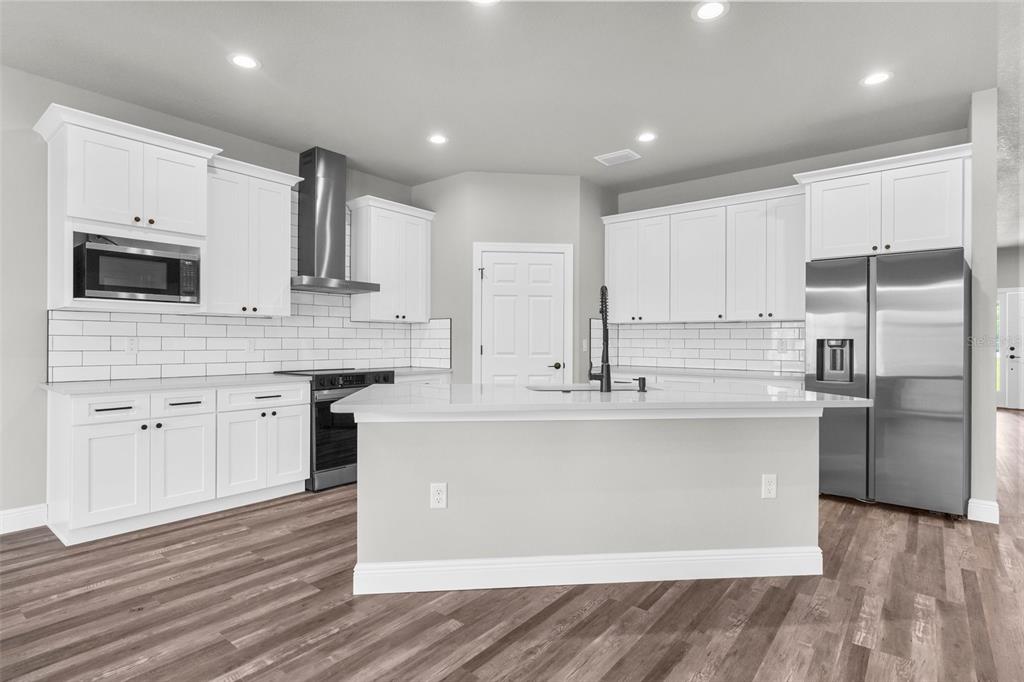 A modern kitchen features white cabinets, stainless steel appliances, a center island, and wood flooring — 16113 PENN STATE ROAD, WEEKI WACHEE, FL