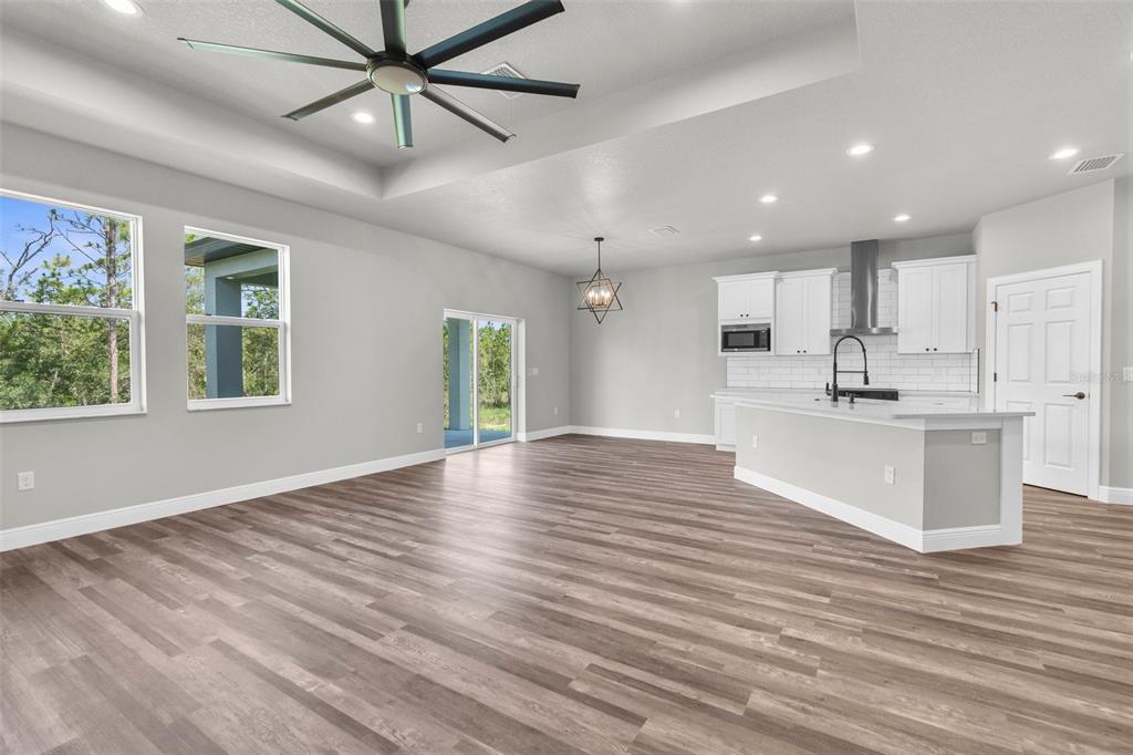 An open-concept kitchen and living area features light gray walls, wood-look flooring, and white cabinetry — 16113 PENN STATE ROAD, WEEKI WACHEE, FL