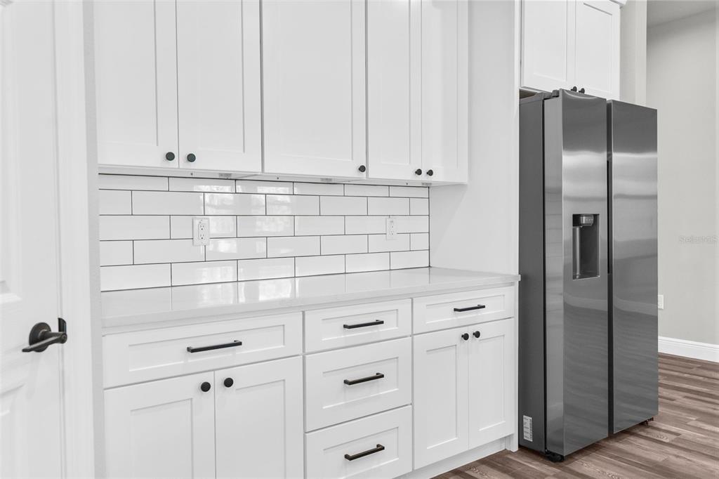 A kitchen area features white cabinets, a subway tile backsplash, and a stainless steel refrigerator — 16113 PENN STATE ROAD, WEEKI WACHEE, FL