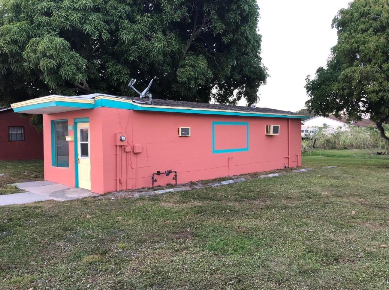 A small, pink, single-story building with a flat roof and turquoise trim sits on grass — 1806 Ave D, Fort Pierce FL 34950, FORT PIERCE, FL