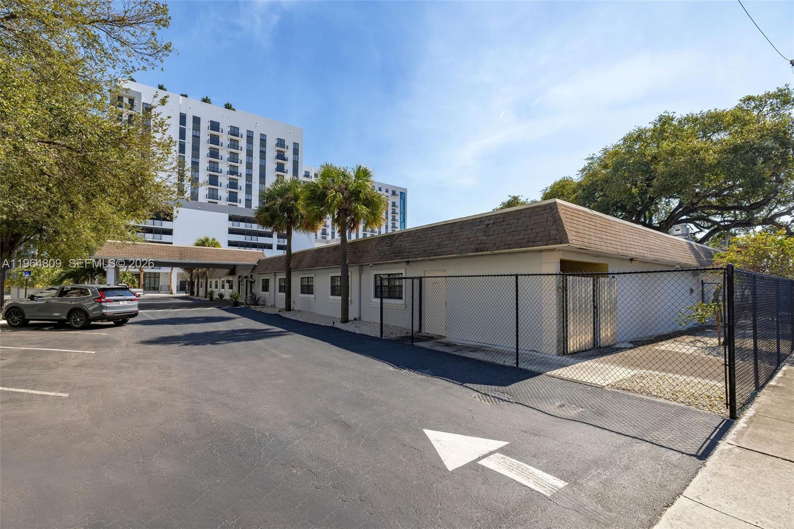 A low-rise building with a brown roof stands next to a parking lot and fence — 151 SW 1st St, Dania Beach FL 33004, DANIA BEACH, FL