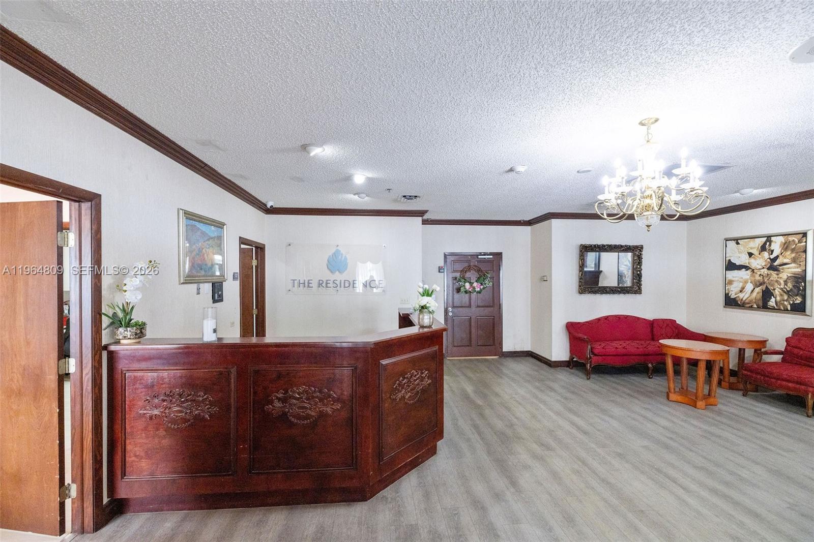 A lobby features a wooden reception desk, red seating, a chandelier, and wood-look flooring — 151 SW 1st St, Dania Beach FL 33004, DANIA BEACH, FL