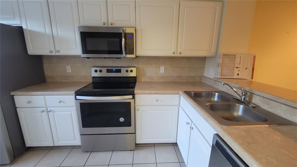 A kitchen features white cabinets, stainless steel appliances, a double sink, and beige countertops — 4316 NW 48TH UNIT 106, GAINESVILLE, FL