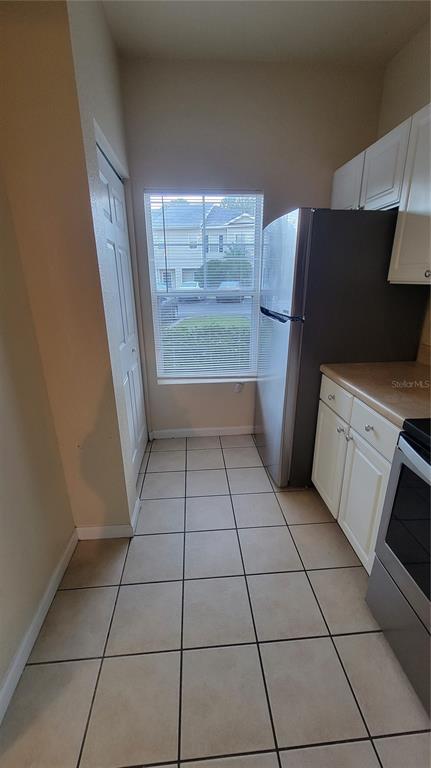 A kitchen features white cabinets, a stainless steel refrigerator, tiled flooring, and a window — 4316 NW 48TH UNIT 106, GAINESVILLE, FL