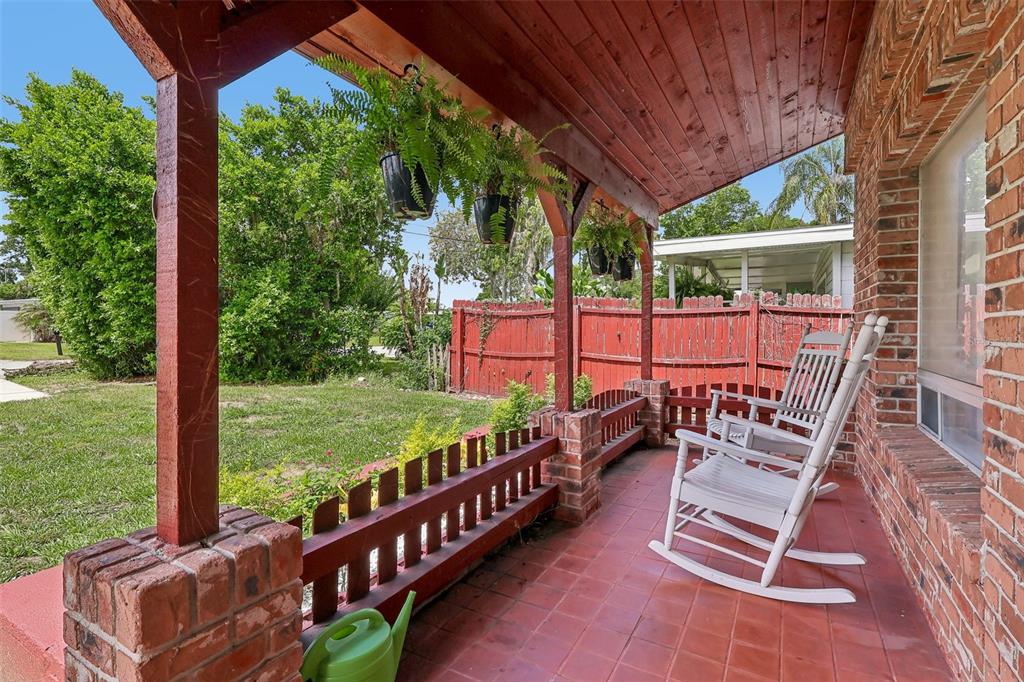 A covered brick porch features two white rocking chairs, hanging ferns, and a red fence — 4301 MIZELL STREET, ORLANDO, FL