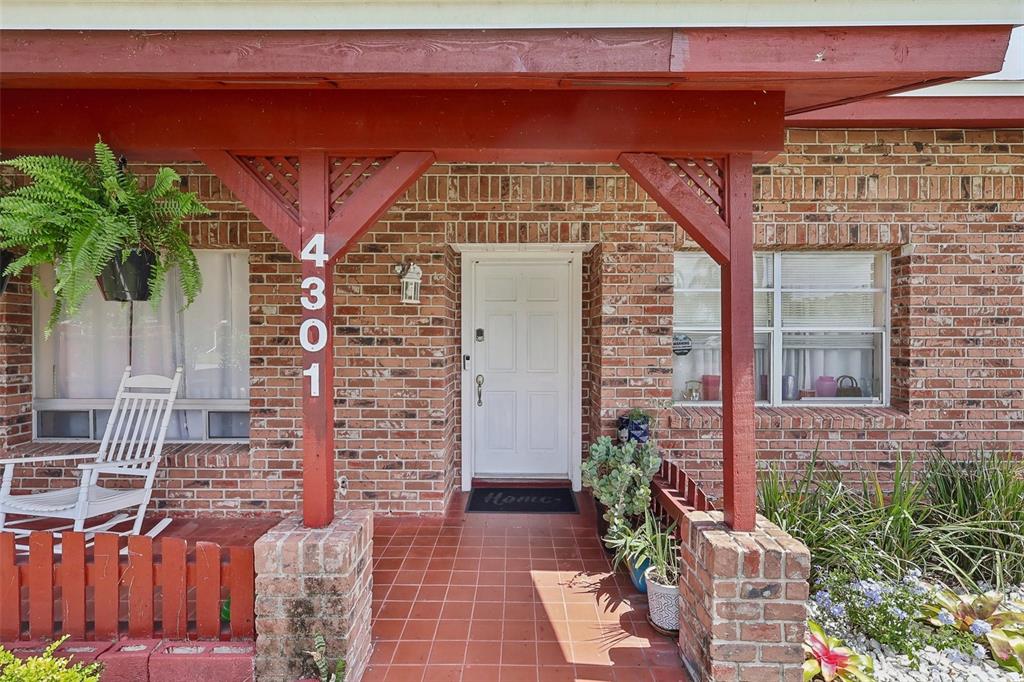 A brick house exterior features a covered front porch with a white door and rocking chair — 4301 MIZELL STREET, ORLANDO, FL